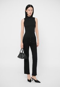 Černý žebrovaný tílko bez rukávů, přiléhavý střih; v kombinaci s černými džíny s vysokým pasem, pěti knoflíky a úzkými nohavicemi. Doplňky zahrnují malou černou kabelku.