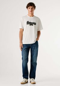 Biele tričko s čiernym nápisom "PEPE JEANS LONDON", doplnené modrými rifľami a bielymi teniskami s čiernymi detailmi.