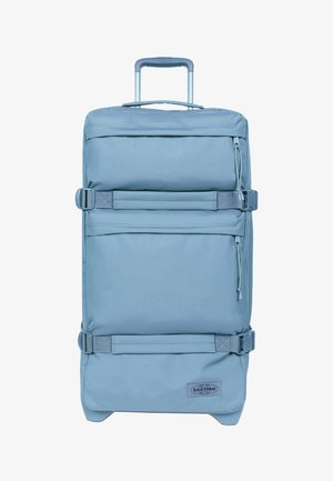 Maleta rectangular de color azul claro con ruedas, asa telescópica, dos bolsillos frontales con cremallera, correas de compresión laterales y parche con el logo de Eastpak en la parte inferior.