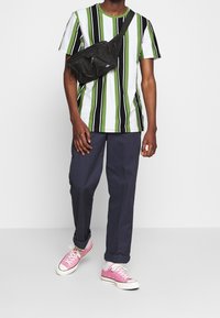 Pasiasta koszulka w zielonym, czarnym i białym kolorze, w zestawie z granatowymi spodniami i różowymi sneakersami. Zawiera czarną torbę na ramię. Odebranie codziennego stylu.