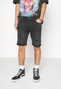 Pantalones cortos de denim negro con un diseño desgastado, con puños enrollados, combinados con zapatillas negras de caña alta y calcetines blancos. Camiseta gráfica con un motivo de tigre.
