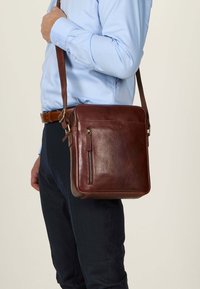 Borsa messenger in pelle marrone con tasca frontale con cerniera e strap regolabile, caratterizzata da una texture liscia e forma quadrata.