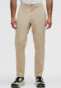 Beige színű, egyenes szabású nadrág, sima, könnyű anyagból készült. Gombos záródással és oldalsó zsebekkel rendelkezik. Fekete-fehér sportcipőkkel viselve.