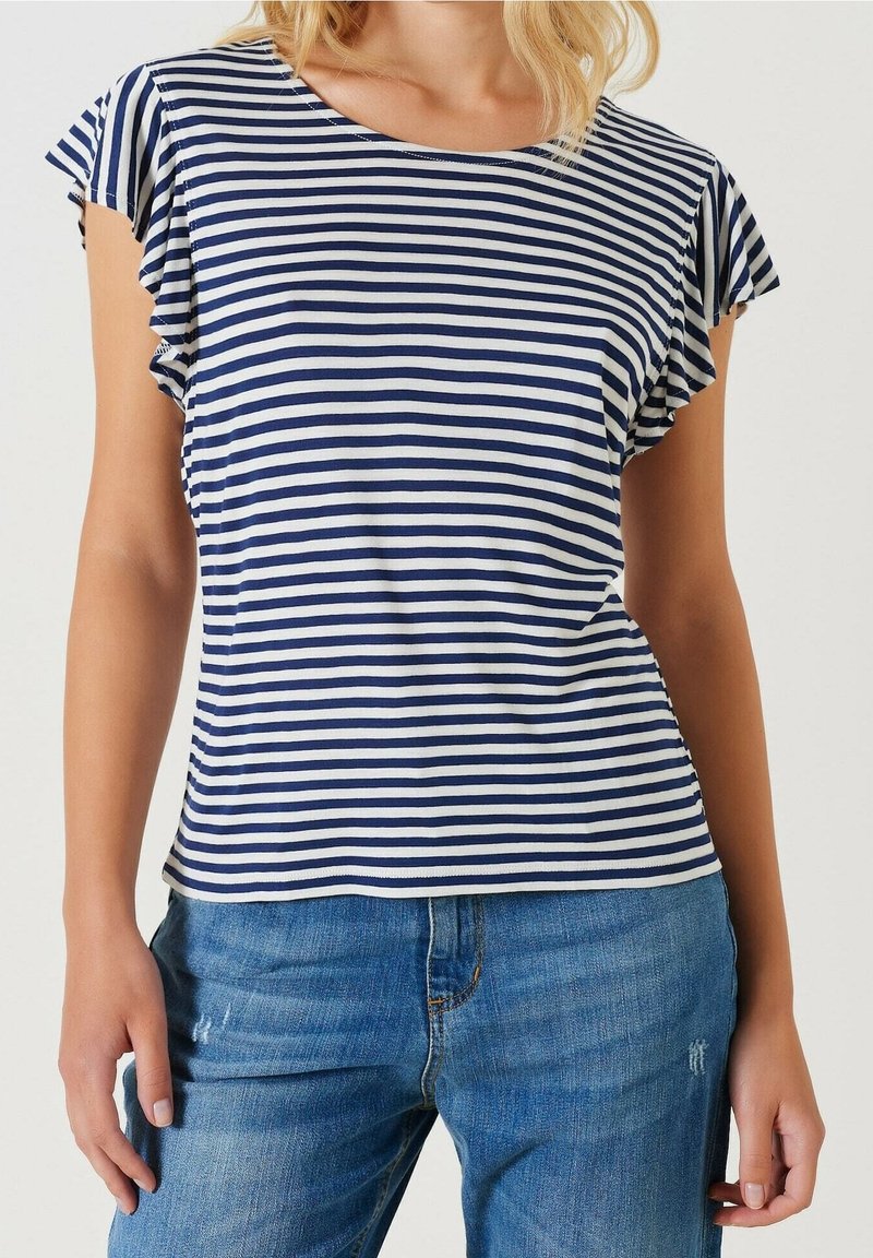 Femme portant un haut à manches courtes rayé bleu marine et blanc avec des manches volantées, associé à un jean bleu en denim.