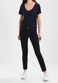 Mörkblå kortärmad t-shirt i kombination med mörka skinny jeans. Modellen bär vita sneakers. Enkelt design, mjuk textur och figurnära passform.