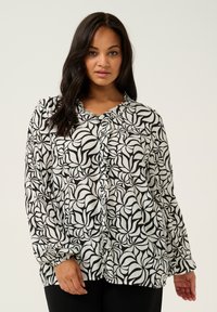 Blouse à motifs noir et blanc avec un col froncé et une fermeture à boutons. Manches longues avec des poignets élastiques et une coupe décontractée.