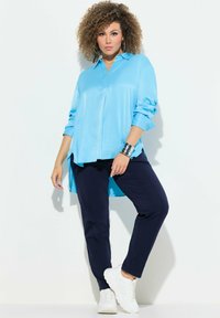 Camicia a maniche lunghe azzurra, in tessuto liscio, con bottoni, abbinata a pantaloni blu navy e sneakers bianche. Bracciale in argento come elemento decorativo.