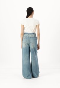 Jeans din denim cu picioare largi, de culoare albastru deschis, cu un elastic înalt și două buzunare la spate. Textură netedă cu un efect subtil de ombre pe picioare.