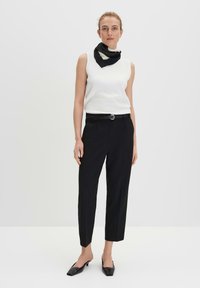 Witte mouwloze top, gestructureerde stof, gecombineerd met zwarte rechte broek, zwarte riem en een zwart-wit gestippelde sjaal. Zwarte puntige ballerina's.