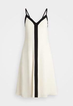 Beżowa sukienka bez rękawów z czarnym wykończeniem w kształcie litery V, cienkimi czarnymi ramiączkami i pionowym czarnym paskiem na środku przodu.
