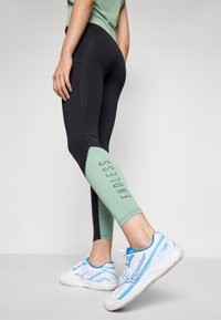 Black and mint-green leggings with "ENDLESS" print, paired with blue and white athletic shoes. Smooth, stretchy fabric.