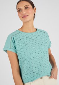 Camiseta de manga corta en azul claro con un patrón perforado. Presenta mangas enrolladas y un escote redondo en un material suave y transpirable.