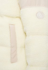 Dikke witte fleece jacksectie met een gladde roze baan, voorzien van een rond logo en een gestructureerd zakdetail. Zacht en warm materiaal.