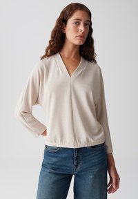 Helles beiges, geripptes Oberteil mit V-Ausschnitt, langen Ärmeln und lockerem Schnitt. Kombinieren Sie es mit blauen Denim-Jeans für einen lässigen Look.
