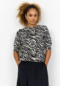 Kortærmet top i beige og sort zebra-stribet mønster, med rund halsudskæring og afslappet pasform, parret med en sort nederdel med elastisk talje.