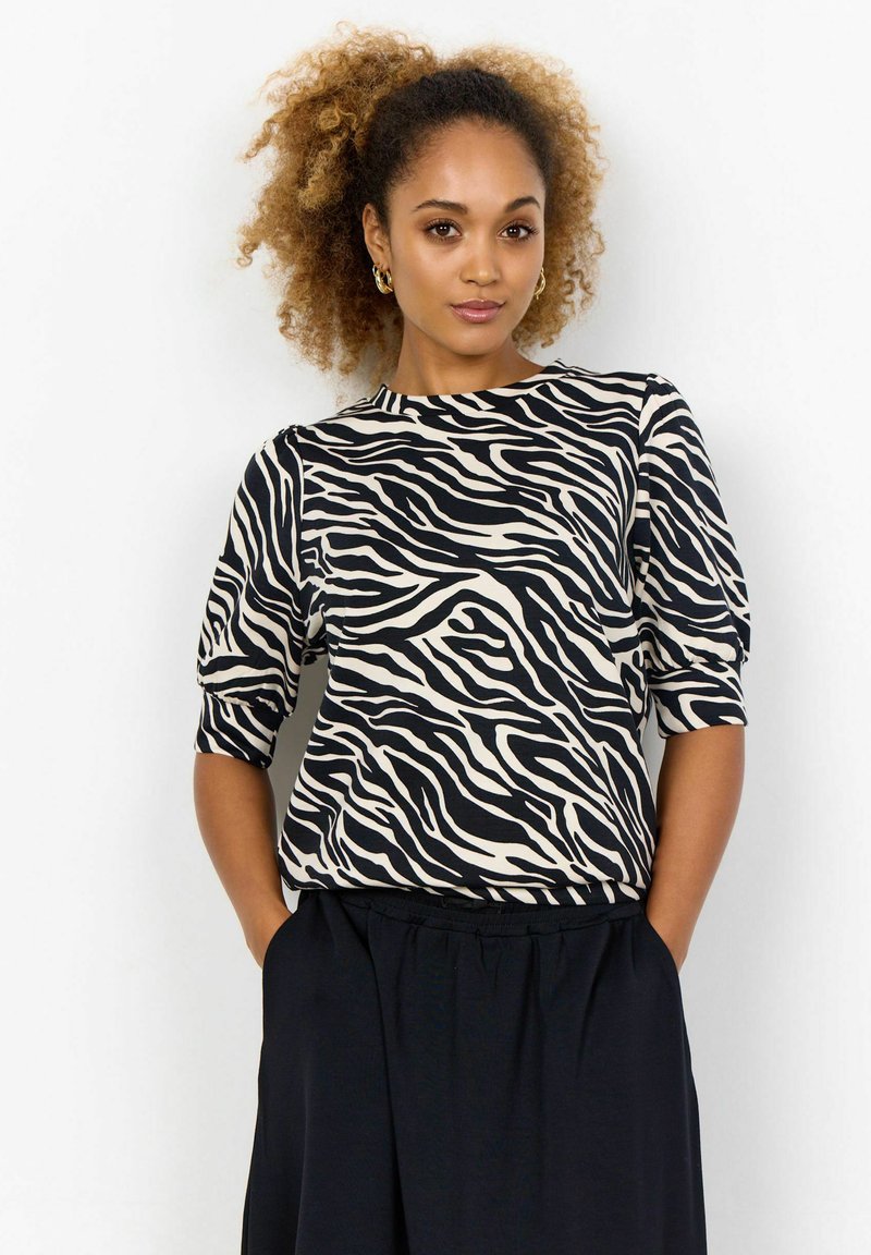 Kortærmet top i beige og sort zebra-stribet mønster, med rund halsudskæring og afslappet pasform, parret med en sort nederdel med elastisk talje.