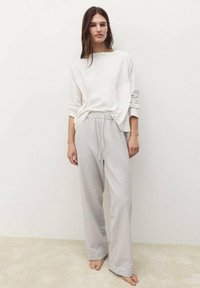 Camicia bianca a maniche lunghe, dalla vestibilità morbida, abbinata a pantaloni larghi a righe grigio chiaro. Tessuto morbido, con cintura elastica.