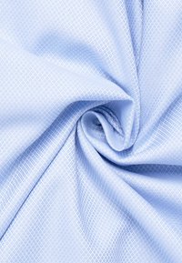 Hellblaue strukturierte Stoff mit einem Diamantmuster, der eine glatte und weiche Oberfläche zeigt, sanft gedreht, um seinen Fall zu betonen.