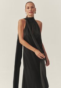 Vestido negro de cuello halter hecho de una tela suave y fluida con un diseño drapeado y un recorte en forma de ojo de cerradura, con un detalle de larga faja.