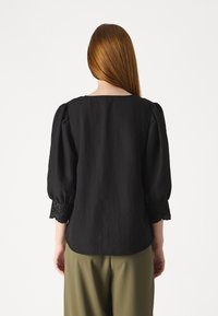 Blusa nera di lino con maniche a sbuffo e dettagli in pizzo ricamato ai polsini. Scollo quadrato e vestibilità rilassata.
