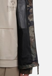 Felpa beige con tasca a marsupio, dotata di un pannello in rete e un motivo camouflage verde e marrone sulla manica.