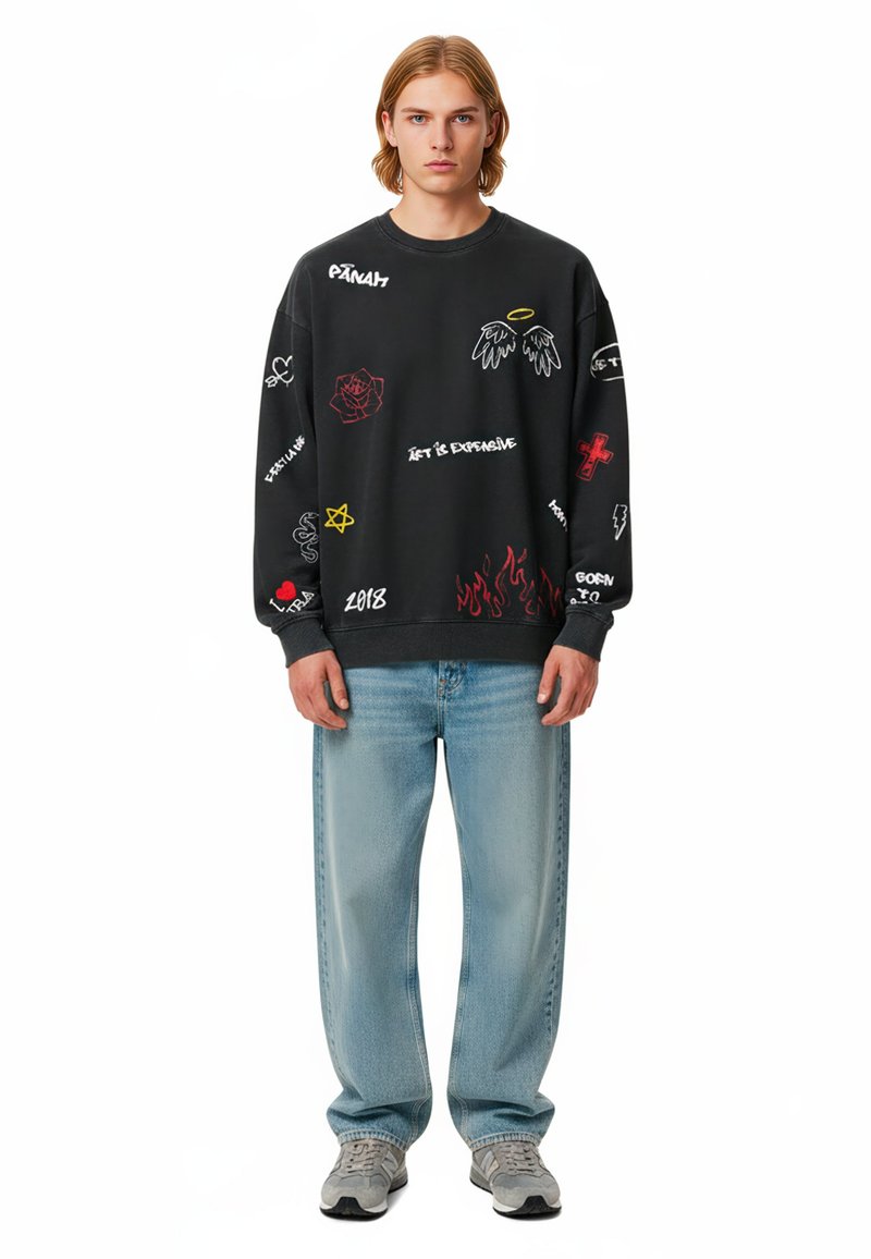 Felpa nera con grafiche colorate e testo. Abbinata a jeans azzurri chiari e sneakers grigie. Taglio casual e stile rilassato.