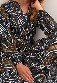 Robe noire à motifs multicolores avec un col en V, des manches longues et une ceinture élastique. Présente des rayures abstraites, des taches et des points.