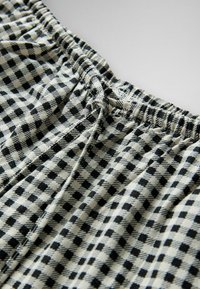 Zwart-wit geruit stof met elastische tailleband en gestrikte trekkoorden, in close-up weergegeven om textuur en patroon te benadrukken.