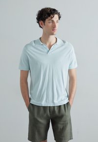 Tricou polo cu mâneci scurte de culoare albastru deschis, cu guler, asortat cu pantaloni scurți de culoare verde măsliniu. Material moale, croi lejer și design minimalist.