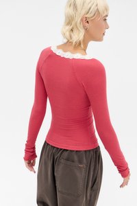 Blusa de manga longa, com riscas, em rosa, com um acabamento de renda branca na gola, design justo; combinada com calças largas, castanhas escuras.