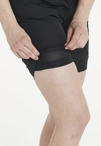 Svarta träningsshorts med mesh-detaljer, med slät tyg och en figurnära design. Sömmen är något uppvikt för att avslöja inre detaljer.