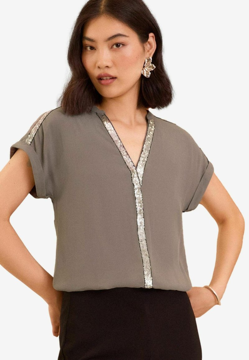 Blusa grigia a maniche corte con scollo a V, dotata di un bordo di paillettes lungo lo scollo e le maniche. Tessuto morbido, vestibilità comoda, design minimalista.