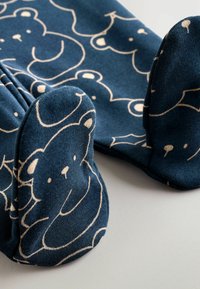 Blaue Fußpyjamas mit einem ganzflächigen Bärenmuster in Creme, mit runden bärenförmigen Füßen und weicher Textur.