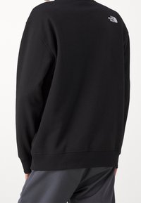 Sudadera negra con un cuello redondo y puños acanalados. Presenta un pequeño logo blanco en la parte superior de la espalda. Está hecha de una suave mezcla de tejidos.