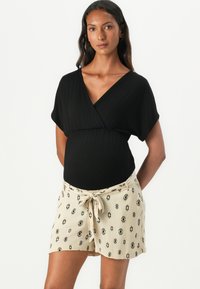 Haut noir à manches courtes associé à un short beige clair avec un motif en losanges noirs et une taille nouée.