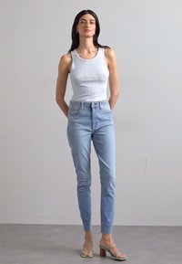 Világoskék, slim fit farmernadrág, fehér bordázott trikóval és zöld, pántos szandállal, amelynek tömbsarkai vannak.
