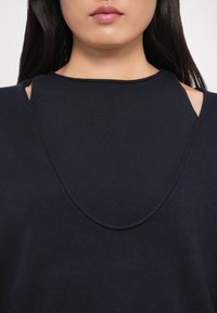 Maglione blu navy con una texture a coste, caratterizzato da dettagli delle spalle a taglio e un colletto rotondo. Tessuto morbido e vestibilità rilassata.