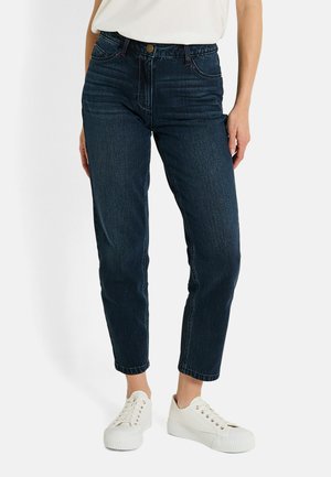 Jeans de denim azul oscuro con un corte relajado, cintura alta y piernas ajustadas. Presentan bolsillos frontales y cierre de botón. Combinados con zapatillas blancas.
