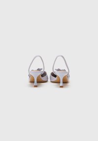 Sandales à talons blancs avec un design élégant, un dos ouvert et des accents floraux sur les sangles. La hauteur du talon est modérée.