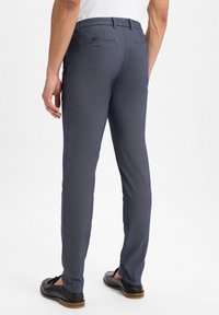 Marineblaue Hose aus strukturiertem Stoff, Slim Fit, mit Gesäßtaschen und Gürtelschlaufen, kombiniert mit schwarzen Schuhen.