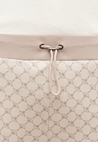 Beežikirju kangas kreemika kudumiga vöökohal, millel on metallist auk ja keskel sõlmitud kreemjas paelalõng.