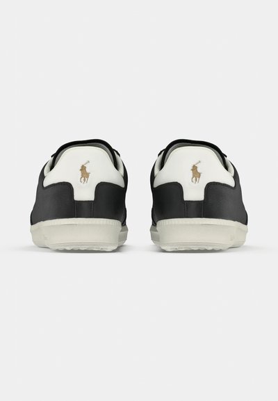 Čierne kožené tenisky s bielymi detailmi, pohľad zozadu. Obsahujú logo na päte, textúrovanú podrážku a okrúhly tvar špičky.