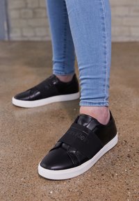 Baskets en cuir noir avec semelles en caoutchouc blanc, dotées d'une bande élastique sur le dessus et d'une finition texturée.