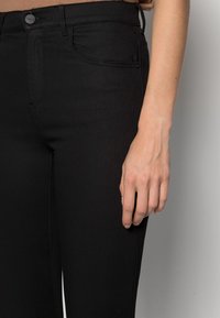 Nedre bild av en person som bär svarta högmidjade skinny jeans med en synlig hand som vilar vid sidan.