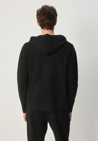 Hanorac negru cu gât rotund și glugă mare reglabilă. Confecționat dintr-un material moale cu o textură fină. Stilizat cu mâneci lungi.