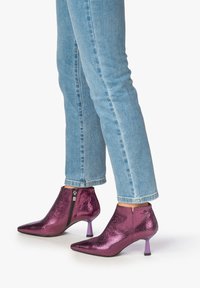 Metalen magenta enkellaarsjes met een puntige neus en een gestructureerde afwerking. Voorzien van een zijrits en een kleine paarse hak. G gedragen met blauwe spijkerbroeken.