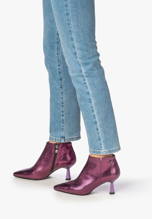 Metallic magenta ankle boots with a pointed toe and textured finish. Features a side zipper and a small purple heel. Worn with blue jeans.