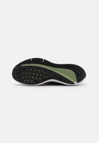 Semelle de chaussure de sport noire et verte avec un motif de prise texturé. Présente un bord blanc proéminent et des accents verts.
