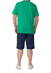 Zielona bawełniana koszulka z krótkim rękawem, w połączeniu z granatowymi szortami i białymi butami wsuwanymi, widok z tyłu. Gładka tekstura, standardowy krój.