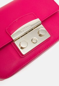 Różowy skórzany portfel z metalicznie srebrną klamrą, z dwoma okrągłymi guzikami i widocznym szwem wzdłuż krawędzi. Logo marki widoczne.